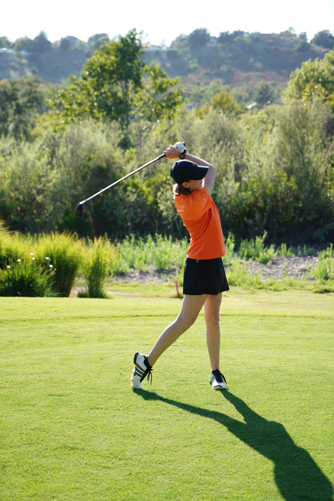 Woman golfer following through on her swing against a bright sky
